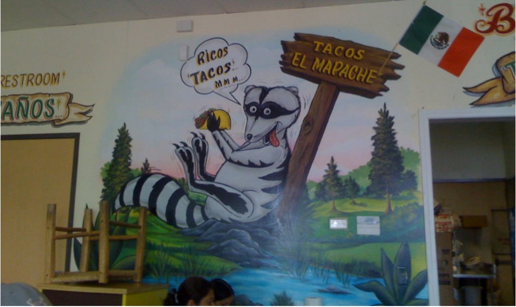 A large raccoon advertises tacos for El Mapache.